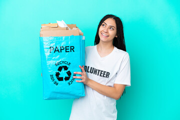 Teenager girl with braids holding a bag to recycle looking up while smiling