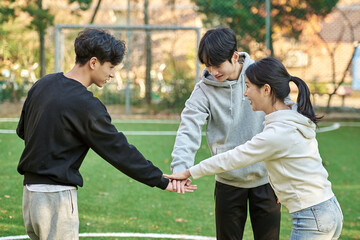 Three young male and female college models walk with a ball and raise their hands in celebration after a game at a fall college futsal field in South Korea, Asia. 