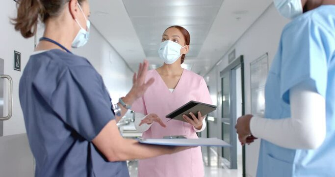 Diverse doctors discussing work and using tablet in corridor at hospital, slow motion