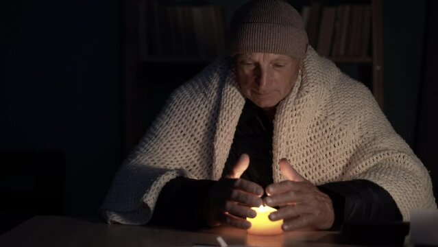 old man hands at home at a table warms his hands from a burning candle. Concept of no heating in winter at home.