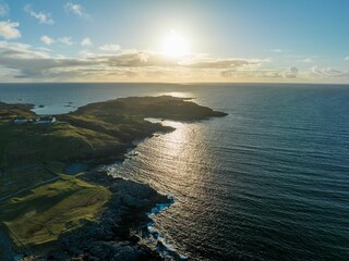 a drone flying over the ocean and shore, at sunset