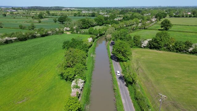 Aerial of a small water canal alongside the green fields and trees on a sunny day