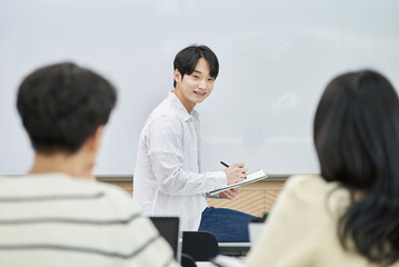 Fototapeta premium An Asian young man is standing in front of a lecture hall at a university in South Korea, giving a presentation or lecture. In front of him are male and female students. 