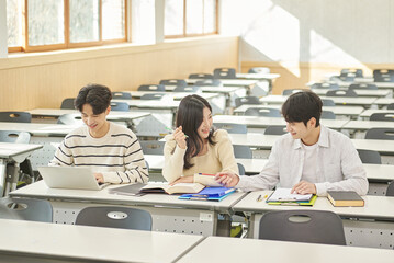 Three young Asian college students, both male and female, are in a classroom in South Korea where they are either teaching or studying