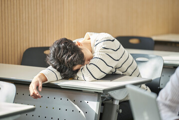 Young college student male model falling asleep on his desk due to tiredness while studying, doing...