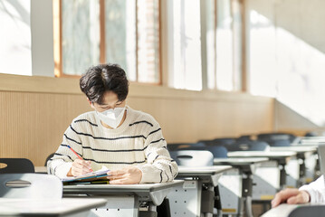 A young university student model wearing a mask while studying in a university classroom in South Korea, Asia during the pandemic.