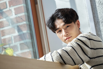 Young male college student models leaning against the wall of a university lecture hall in a light-filled room in South Korea, Asia