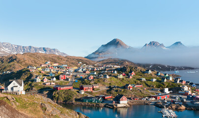 Fototapeta na wymiar A layer of fog spreads between the mountains and the sea -Picturesque village and Colorful houses on coast of Greenland - Tasiilaq, East Greenland