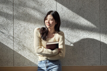 A young female college student model leaning against the wall of a university classroom in a light-filled room in South Korea, Asia.  