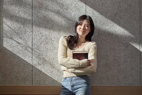 A young female college student model leaning against the wall of a university classroom in a light-filled room in South Korea, Asia.  