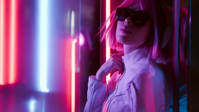 Beautiful woman with purple hair in futuristic costume over dark background. Violet neon light. Portrait of young girl in modern headphones listening music.