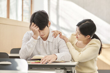 Fototapeta premium Girlfriend comforting a distressed young college male model sitting at a desk in a university classroom in South Korea, Asia