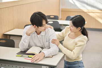 Girlfriend comforting a distressed young college male model sitting at a desk in a university classroom in South Korea, Asia