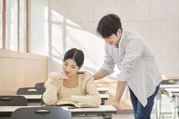 Colleague, friend, motivator, young male model comforting a distressed young female college student model sitting at a desk in a university classroom in Asia Korea.  
