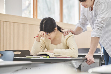 Colleague, friend, motivator, young male model comforting a distressed young female college student model sitting at a desk in a university classroom in Asia Korea.  