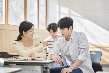 Three young male and female college students models sitting or standing at desks in a university classroom in South Korea, Asia, talking or having a discussion