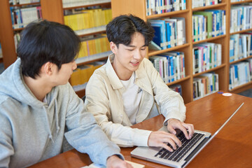 A male student sits at a desk in a university library in South Korea, Asia, looking at a laptop...