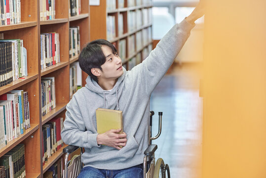 Asia South Korea university library bookcase in a wheelchair looking for a book on the shelf, physically handicapped young disabled male college student model