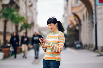 Young japanese woman standing on the boardwalk and typing a message on the phone