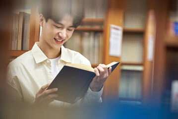 A young man attending college is browsing and reading books on the shelves with different expressions in his university library in South Korea, Asia