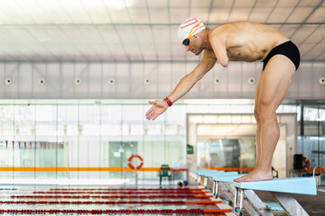 An adult swimmer with an amputated arm is about to jump on the platform of a heated indoor pool. Concept of people with disabilities, athletes with an amputated arm, swimming for the disabled.