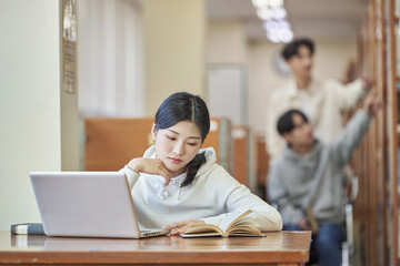 Asian Korean university library desk chair woman sitting on laptop and reading book and man helping...