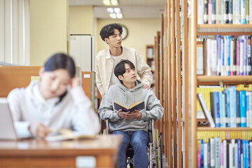 Asian Korean university library desk chair woman sitting on laptop and reading book and man helping disabled man in wheelchair Young Asian male and female models