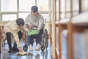 Young handicapped disabled male college student model in wheelchair looking for books in library...