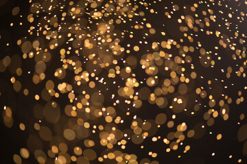 Golden sparks, Christmas and New Year floating littering stars on black bokeh background, backdrop with sparkling gold holiday garland, magic dust, lights. Gold Abstract Glitter Blinking sparks