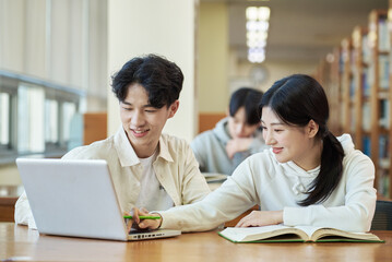 Obraz premium Two young college student man and woman couple model and solo male model looking at laptop and book together in library of Asian Korean university