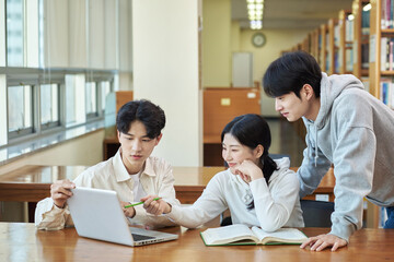 Two young college student man and woman couple model and solo male model looking at laptop and book together in library of Asian Korean university
