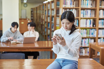 Young Asian Korean female model, male model and bookshelf background looking out the window holding mobile phone in library in library © TEAM PRE-LIGHT
