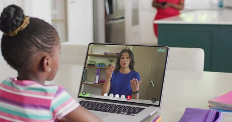 Happy diverse schoolgirl having laptop video call with female teacher in slow motion - Powered by Adobe