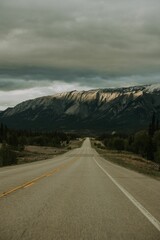 Naklejka premium Winding road stretches through a mountainous landscape, with towering peaks and ominous clouds
