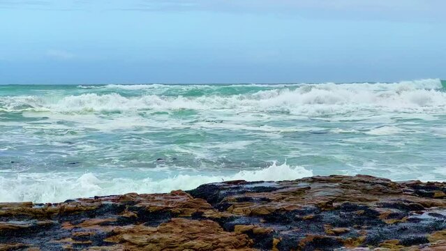 Slow motion of the foamy waves of the sea hitting the rocky shore under the cloudy sky