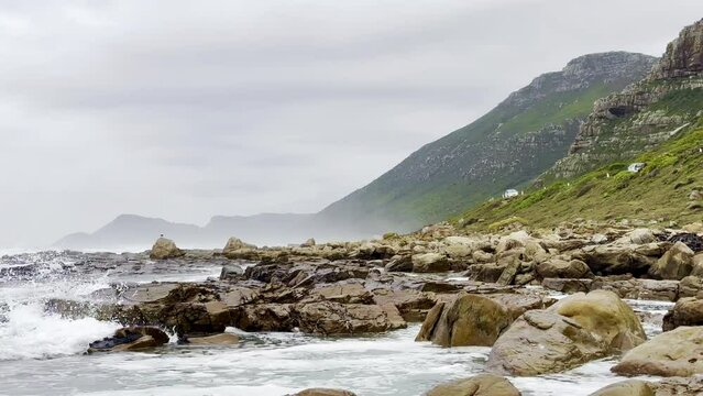 Foamy waves of the sea hitting the rocky shore under the cloudy sky