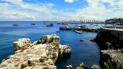 Blick durch Felsen auf Fischereihafen von Cascais in Portugal mit Booten unter blauem Himmel mit...