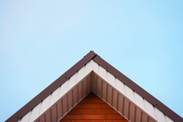 The top of the triangular roof of the house against the sky - Powered by Adobe