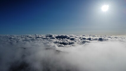 Stunning view of the clouds over the mountains covered in dense trees at sunlight