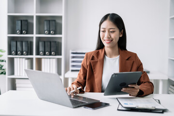 Businesswomen using tablet with laptop and document on desk in modern office.
