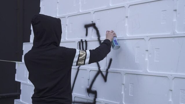 A girl writes graffiti on the wall with the spray