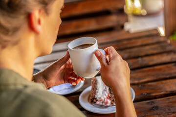 An unrecognizable female person enjoying a first sip of coffe and a piece of cake at a rustic...