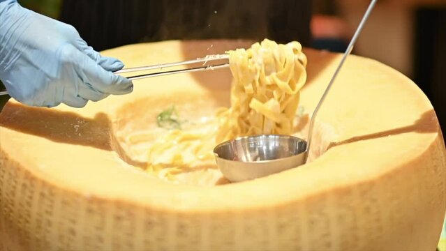 Chef preparing pasta in a big parmesan wheel, slow motion