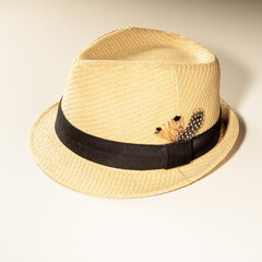 sun hat with a ribbon and a bird feather made of light straw for holidays on a light background