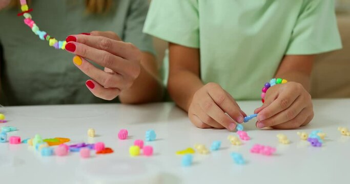 Happy mother with her daughters making beaded jewelry at home