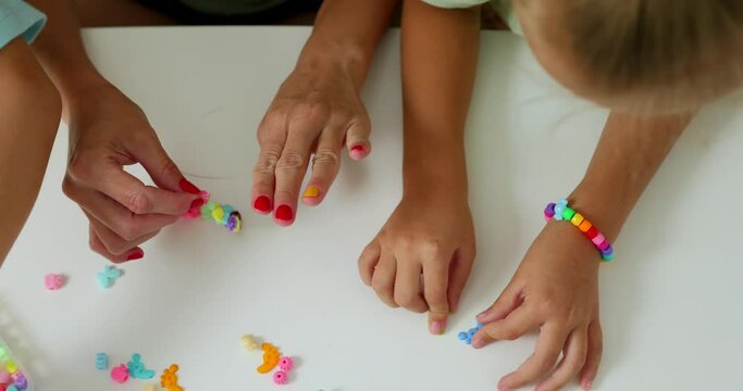 Happy mother with her daughters making beaded jewelry at home