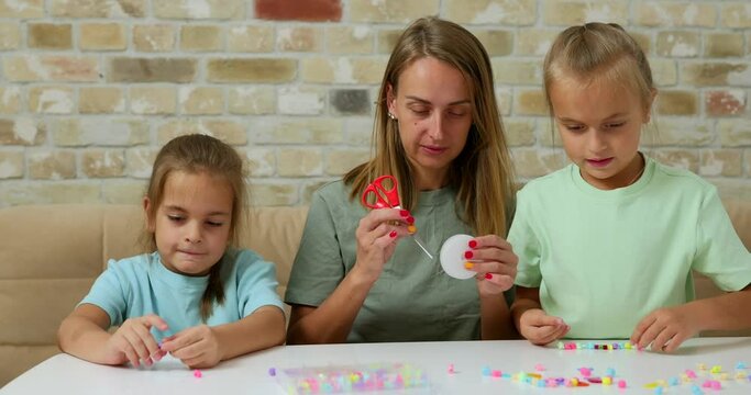 Happy mother with her daughters making beaded jewelry at home