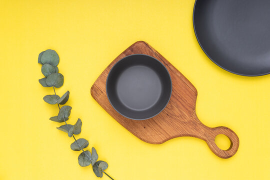 eucalyptus on yellow background, wooden cutting board and black porcelain plates