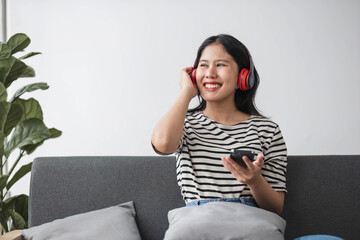 Portrait young asian woman using smart mobile phone with headphone for listen music on sofa