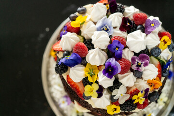 Top down decorated chocolate cake with berries, flowers, meringue and cream